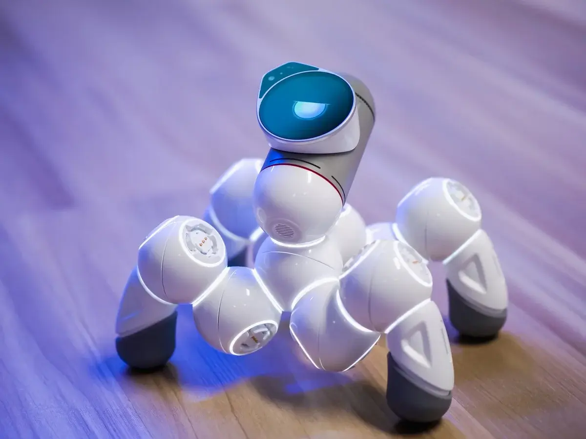 A white robot toy standing on a wooden floor with blue lighting.