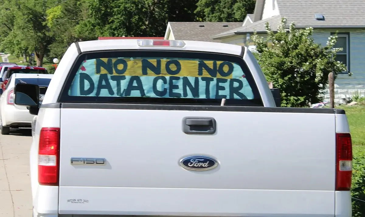 A pickup truck with a rear-window sign reading 'NO NO NO DATA CENTER' parked in a neighborhood.
