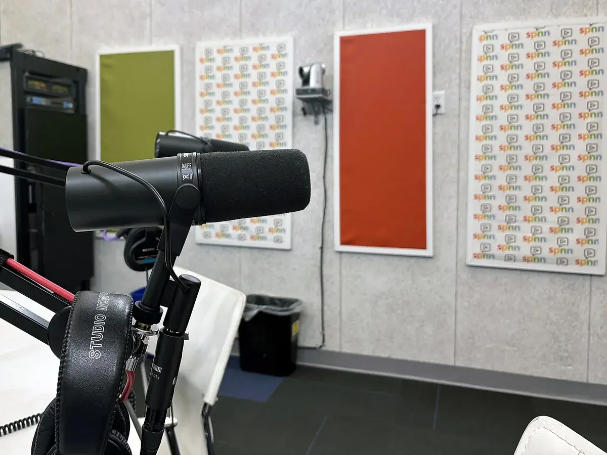 A podcast microphone on a boom arm in a studio with SPNN-branded walls.
