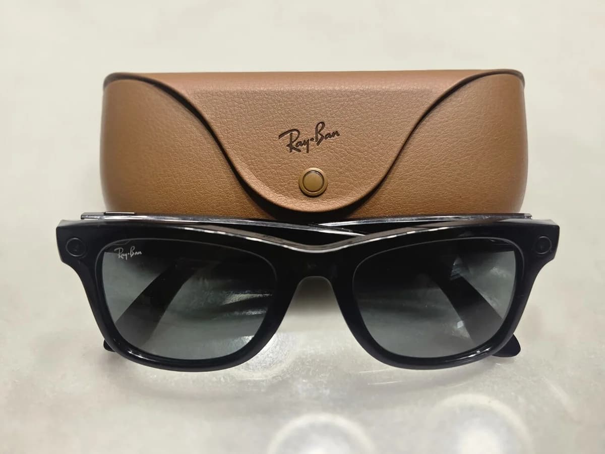 Black Ray-Ban smart glasses in front of a brown leather charging case.