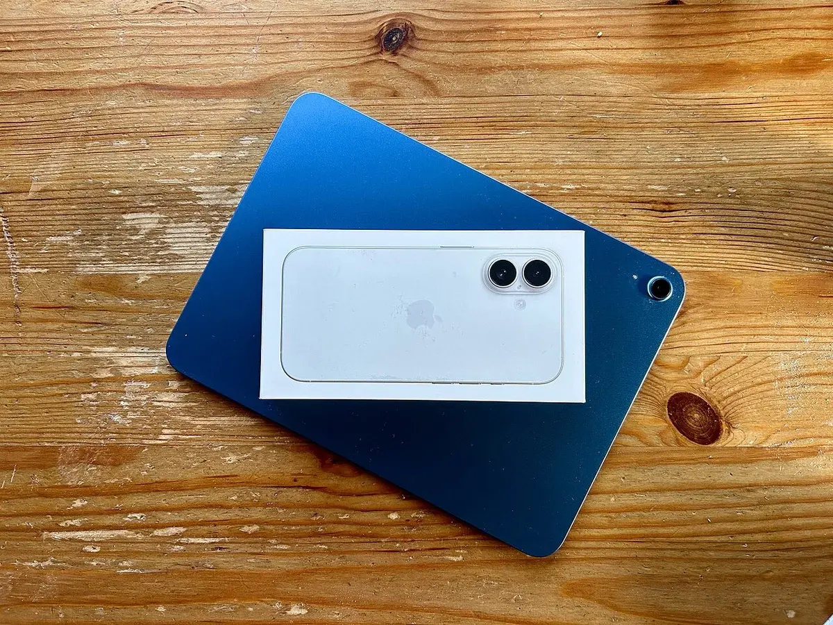 An iPad and an iPhone in their boxes on a wooden table.