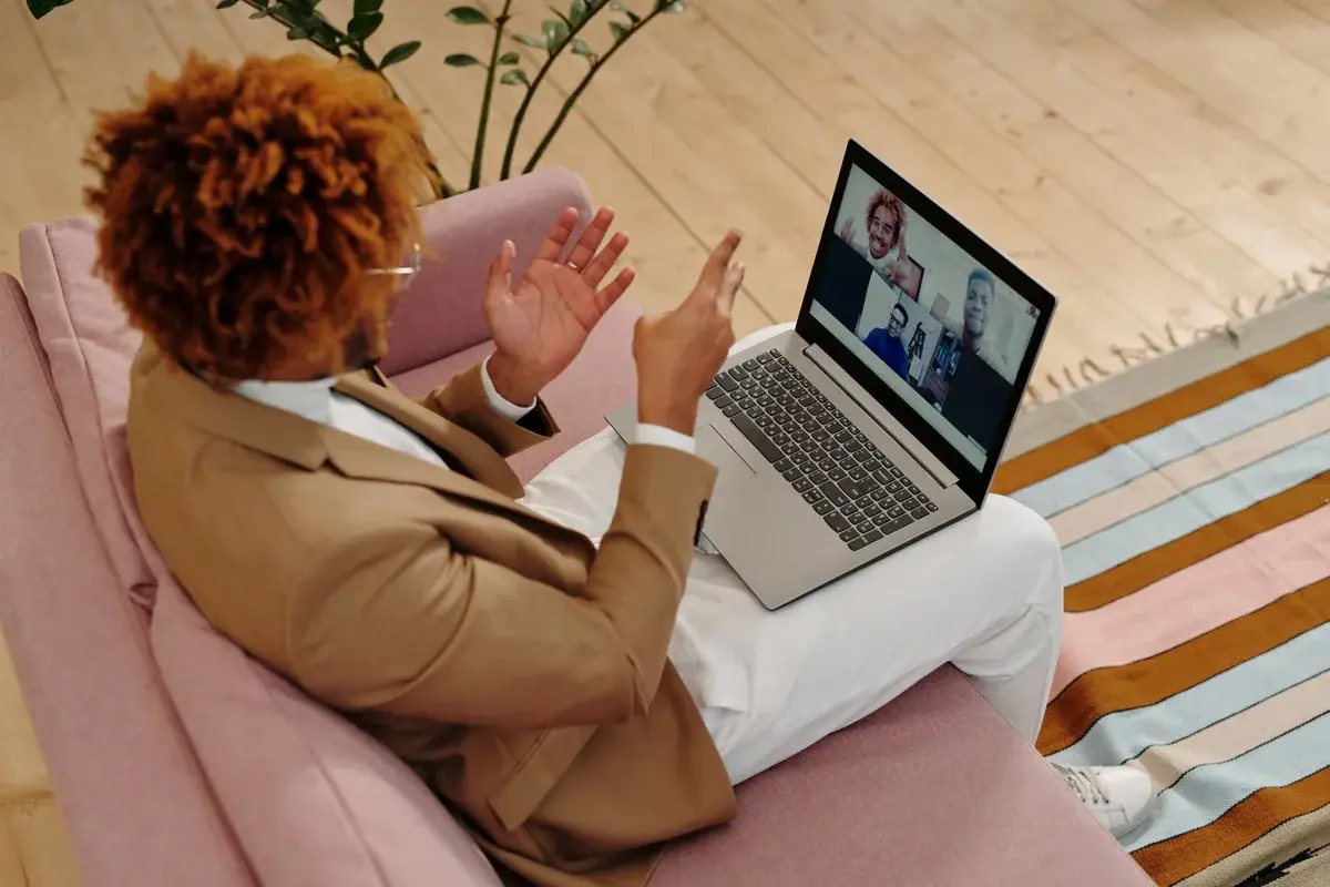 A person in a suit video chatting on a laptop while sitting on a sofa.