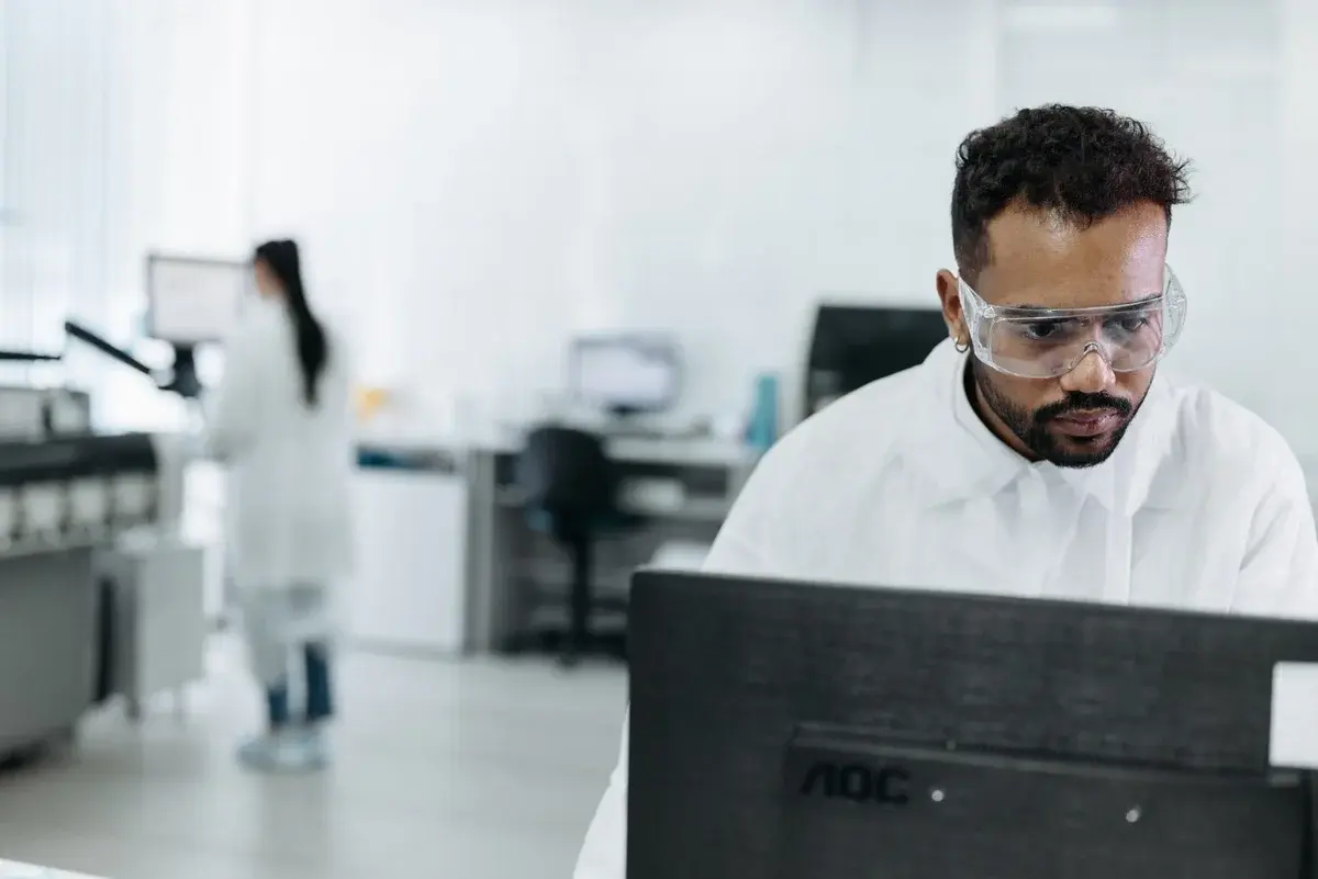A scientist in goggles works at a computer in a lab.