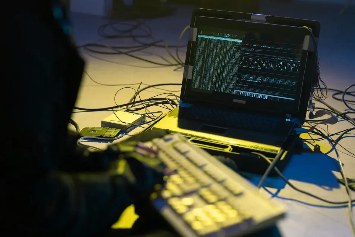 A silhouetted person typing at a keyboard beside a laptop showing code.