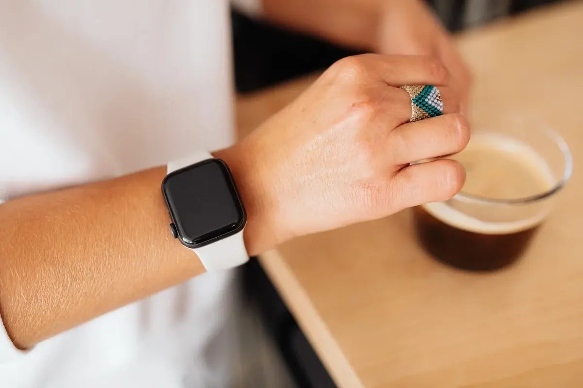 Close-up of a hand wearing a smartwatch beside a coffee cup.