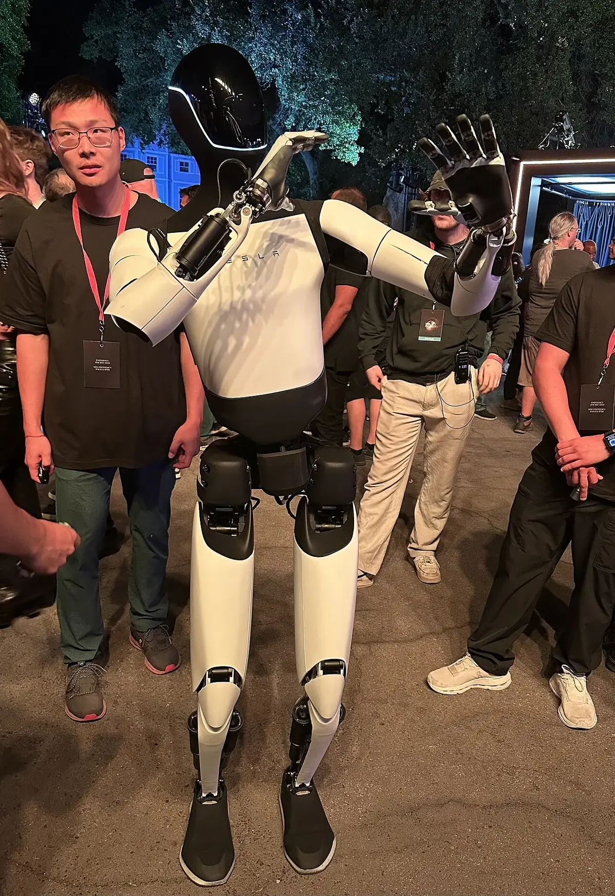 A Tesla Optimus robot standing among people at a nighttime event.