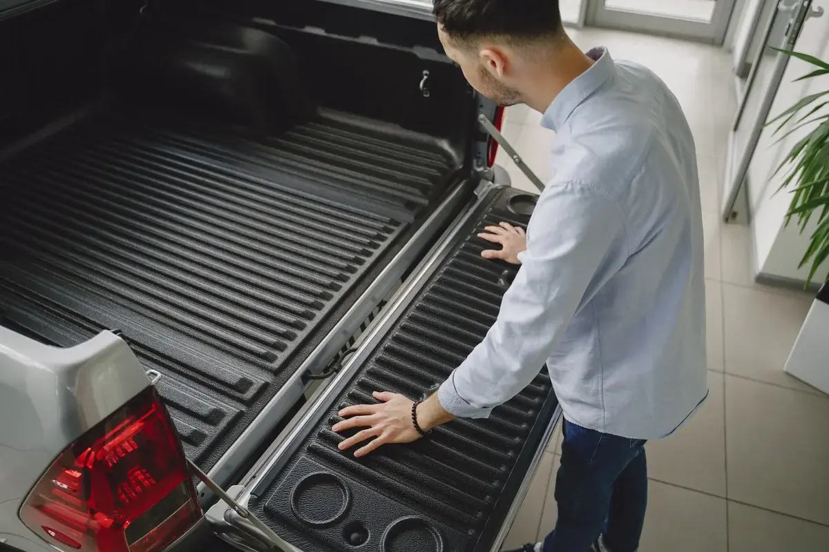 A man examines the open tailgate of a pickup truck in a showroom.