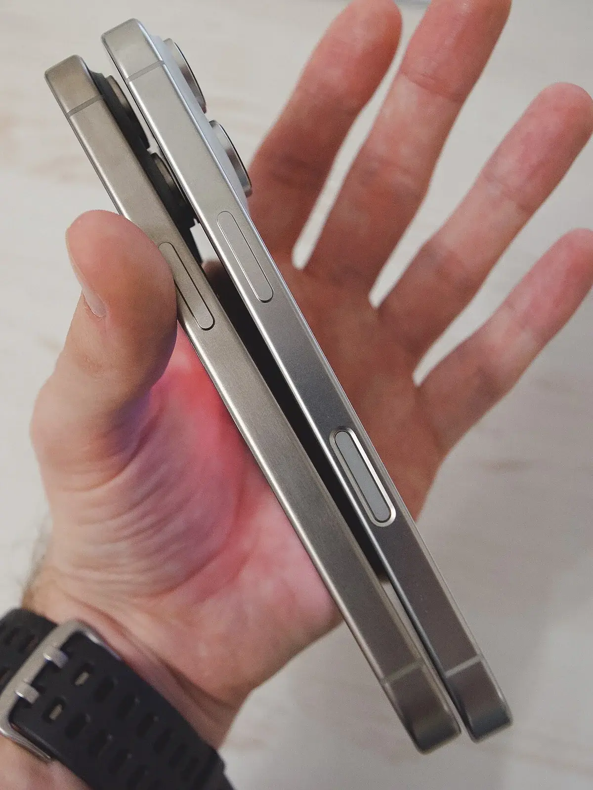 A hand holding two iPhones side by side for size and design comparison.