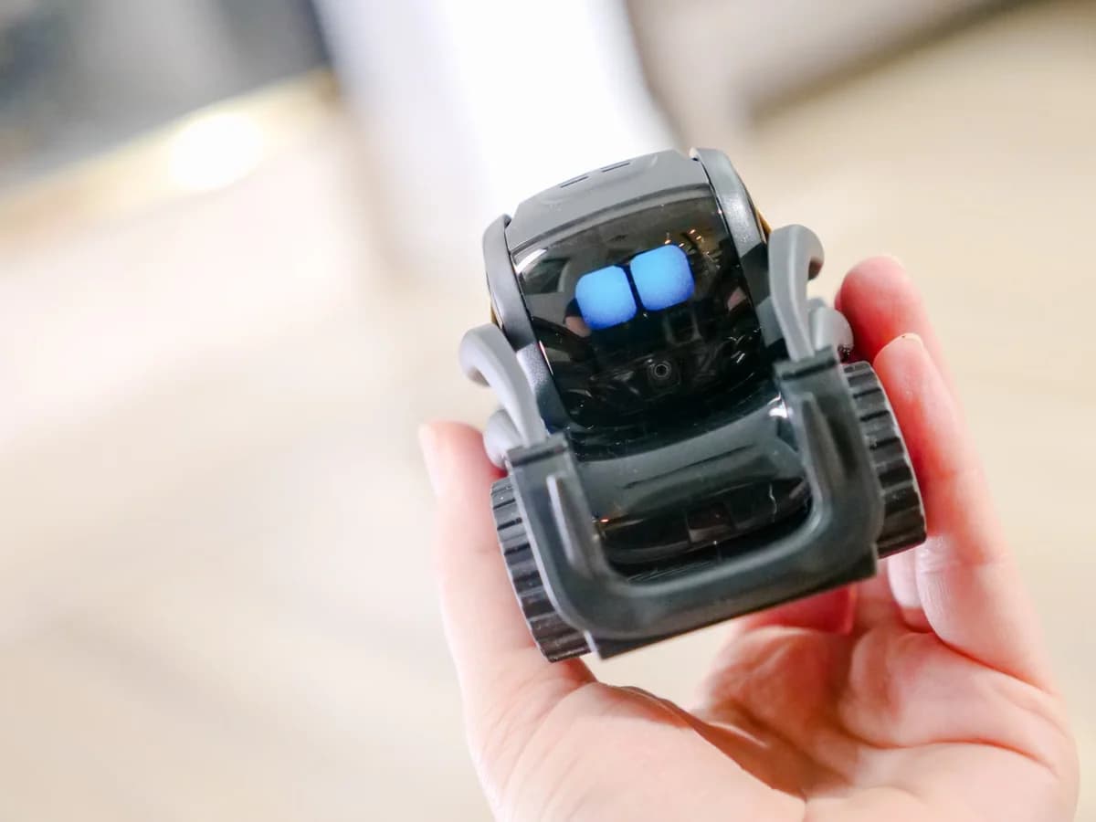 A hand holding a small modern robot.