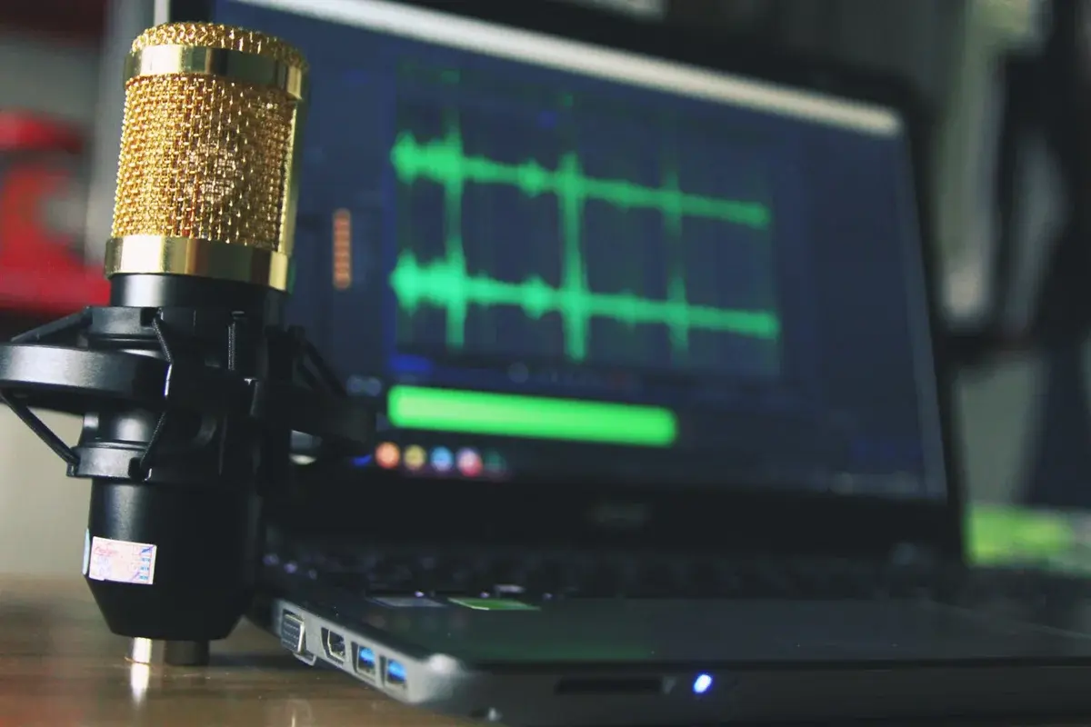 A gold microphone next to a laptop showing audio waveforms.