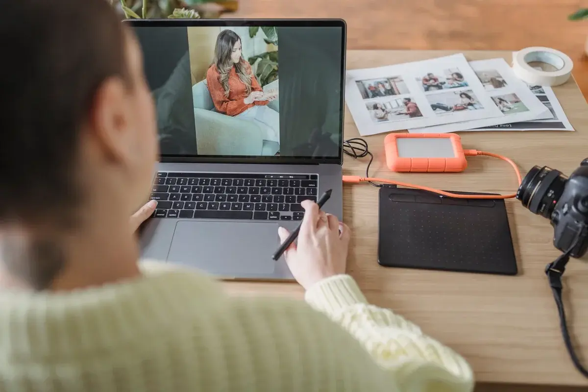 A woman edits photos on a laptop at a desk with a camera and graphics tablet.