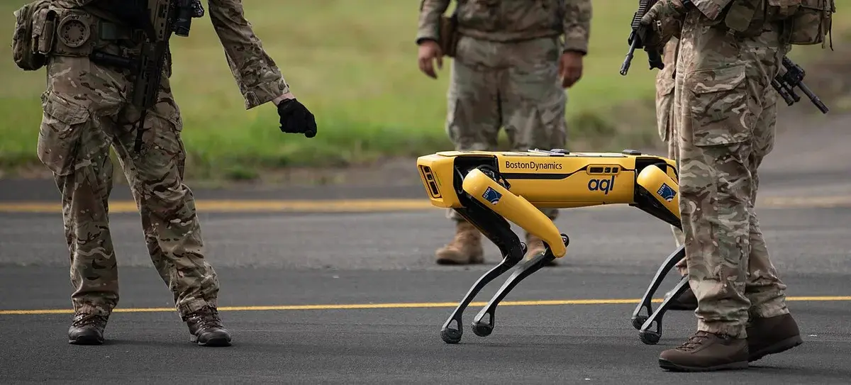 Military personnel standing around a yellow Boston Dynamics Spot robot.
