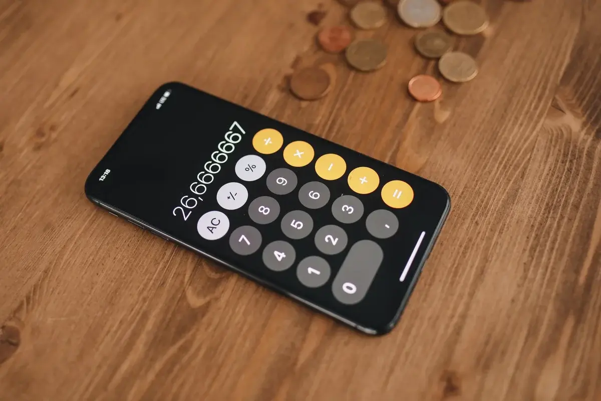 A smartphone with a calculator app on a wooden table next to scattered coins.