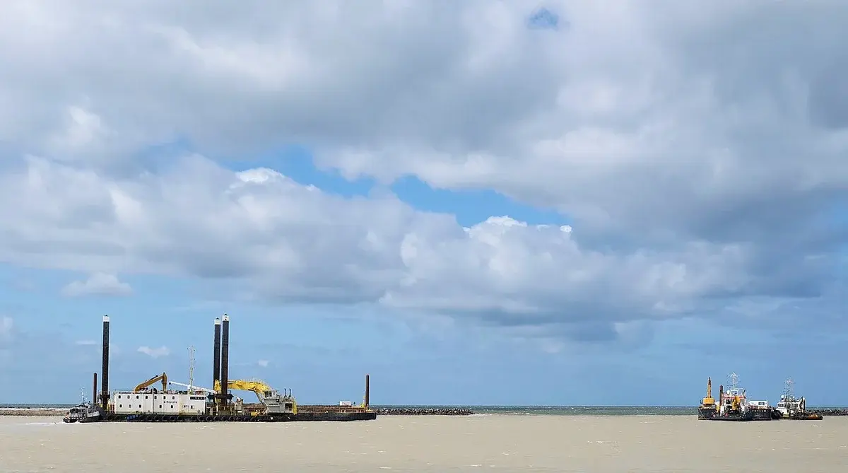 Barges and construction equipment working at sea under a cloudy sky.