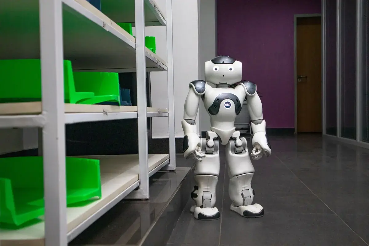 A humanoid robot standing in a corridor next to shelves.