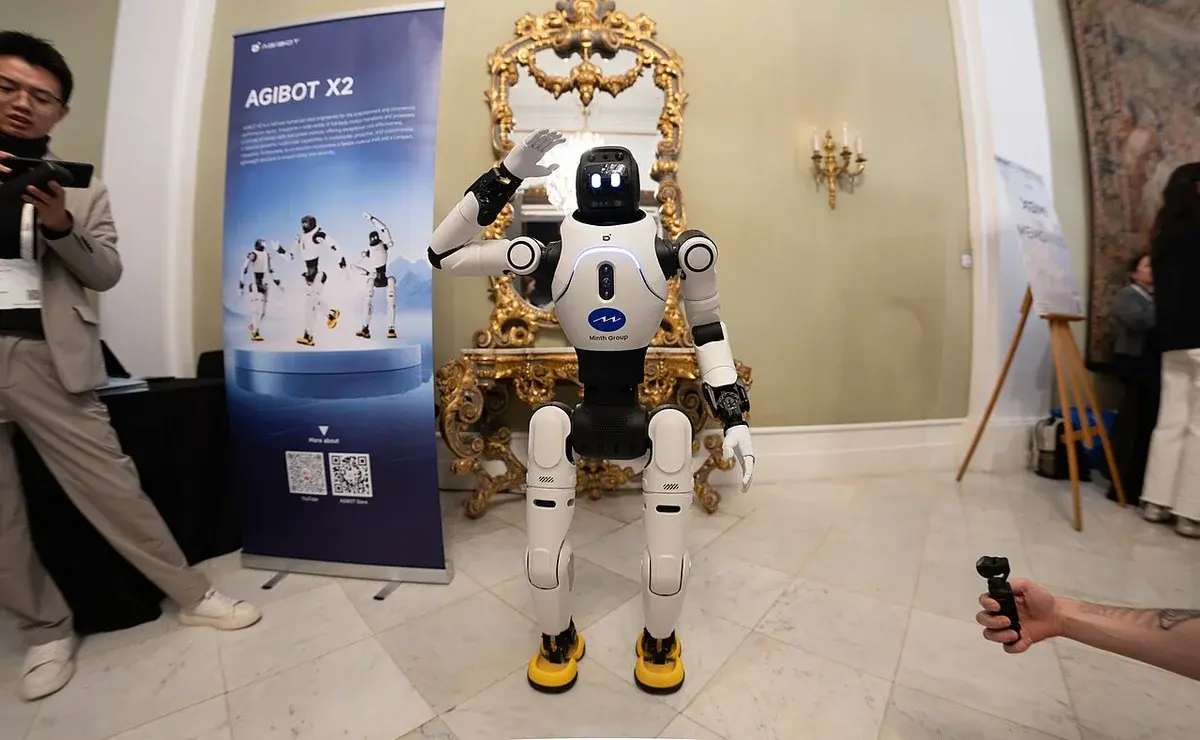 A humanoid robot on display at a tech event, waving to the camera.