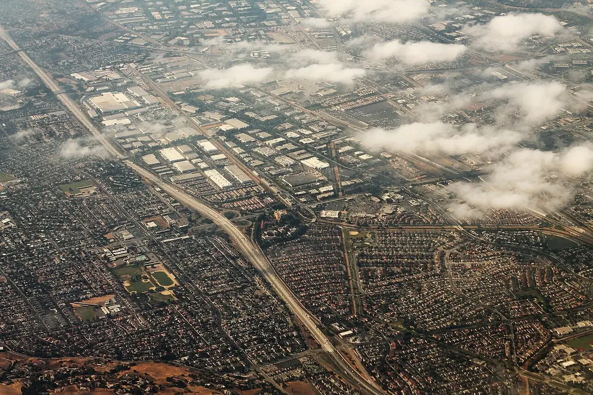 Aerial view of a dense city area with roads, buildings, and clouds.