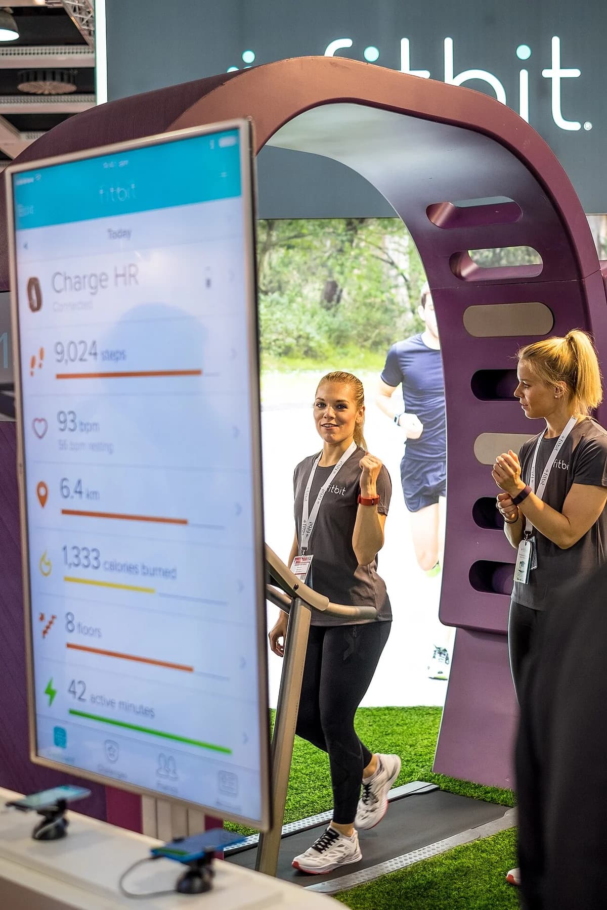Fitbit booth at a technology trade fair with two women and a large app display.