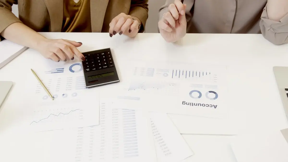 Two professionals reviewing accounting papers and using a calculator at a table.
