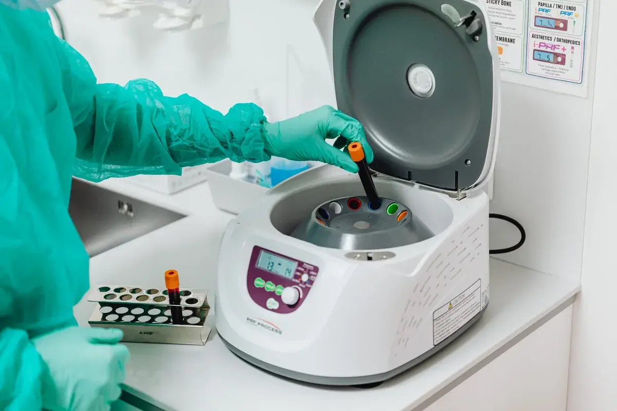 Gloved healthcare worker loading a centrifuge in a lab.
