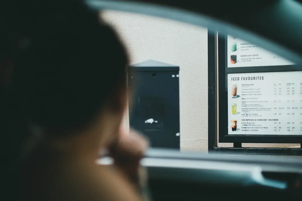 A person ordering coffee at a drive-thru with the menu board visible.