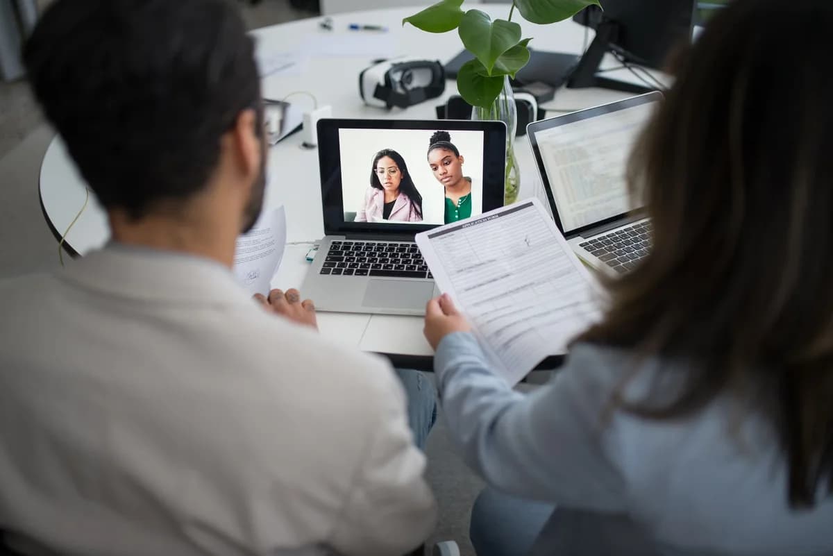 Two people in an office view a virtual job interview on a laptop screen.