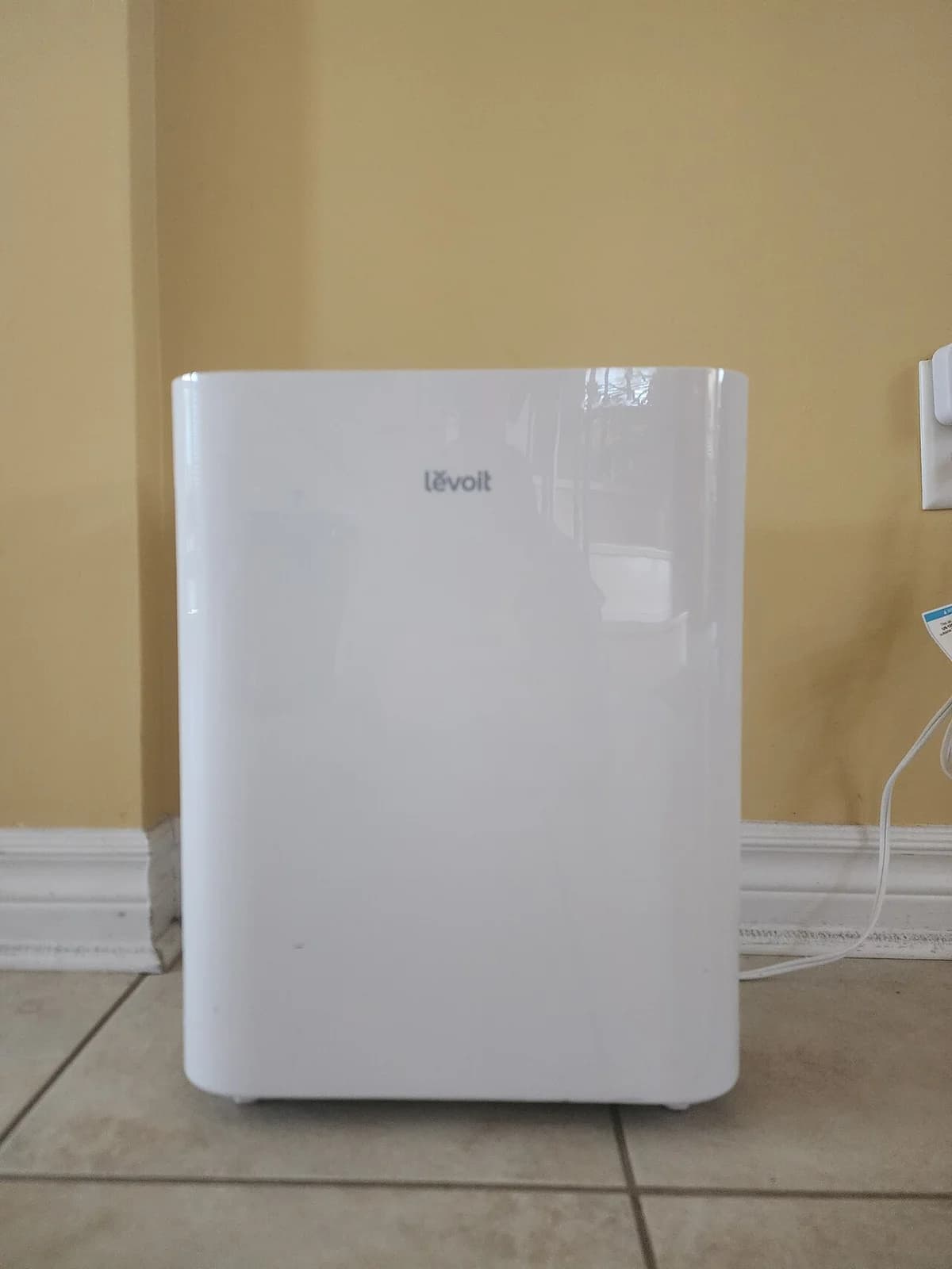 A white Levoit air purifier against a wall.