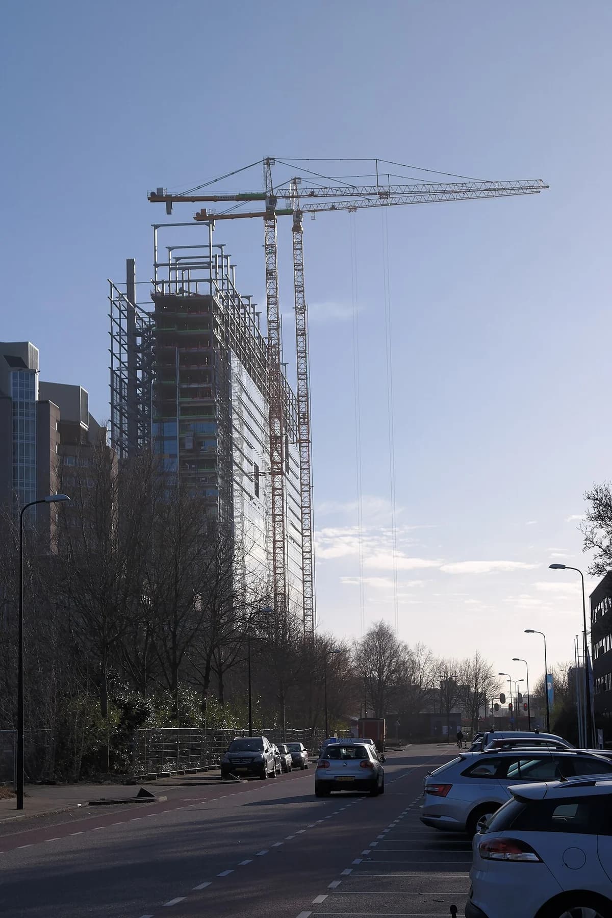 A building under construction with cranes towering above a street.